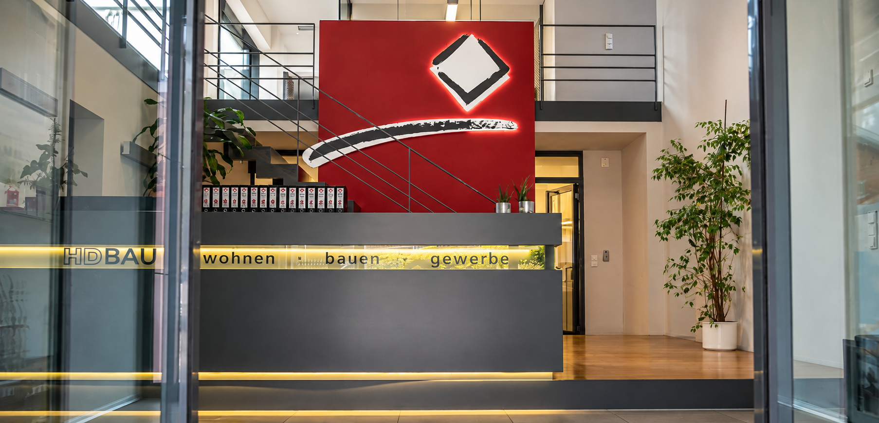 Empfangsbereich der HD-Bau-Zentrale mit hinterleuchtetem Logo auf roter Wand